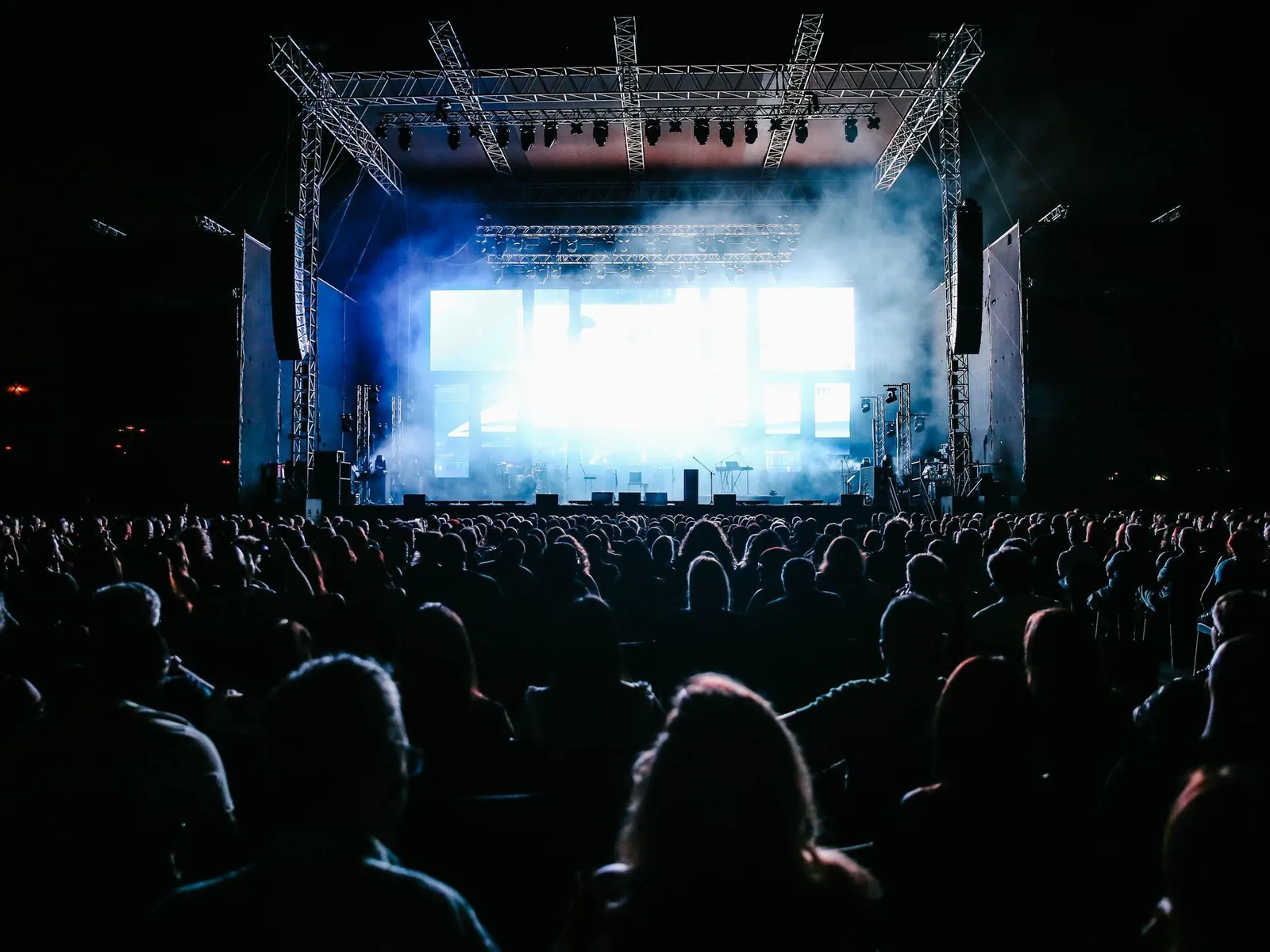 A crowd at an open-air concert at night, hands up in front of a lit stage