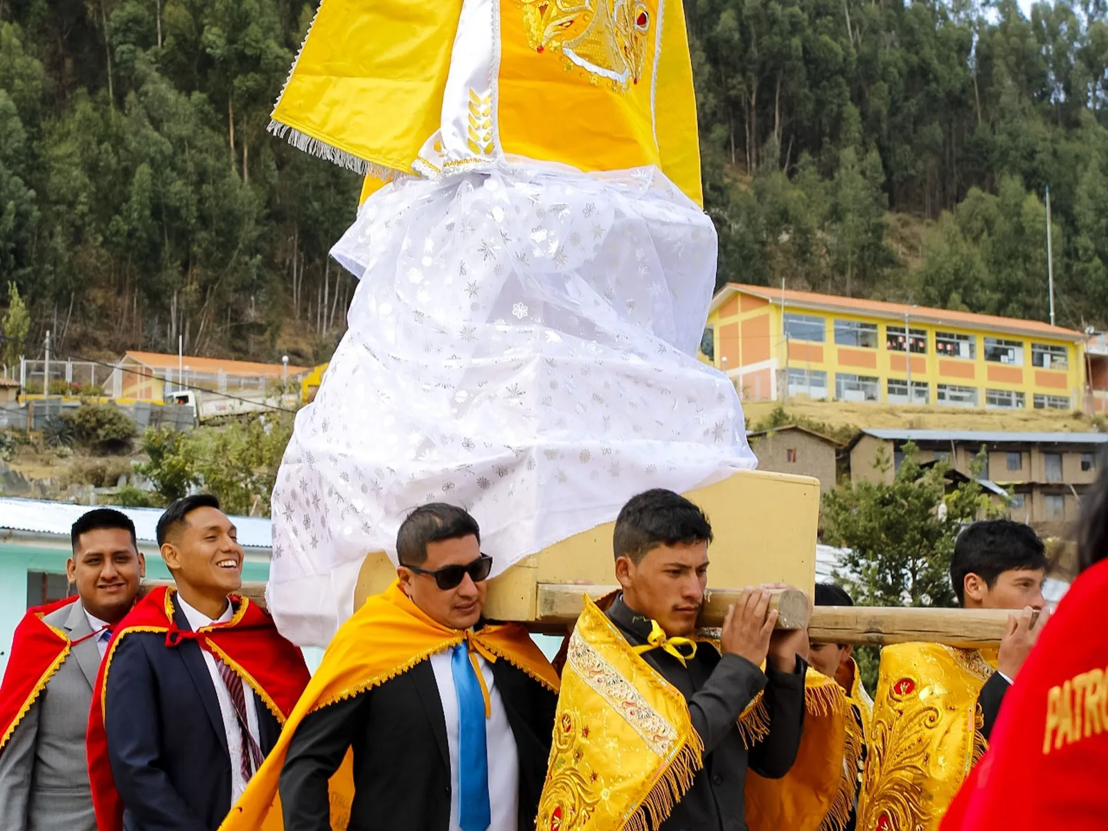 Men carrying an ornate religious statue through a street during a saint’s day procession