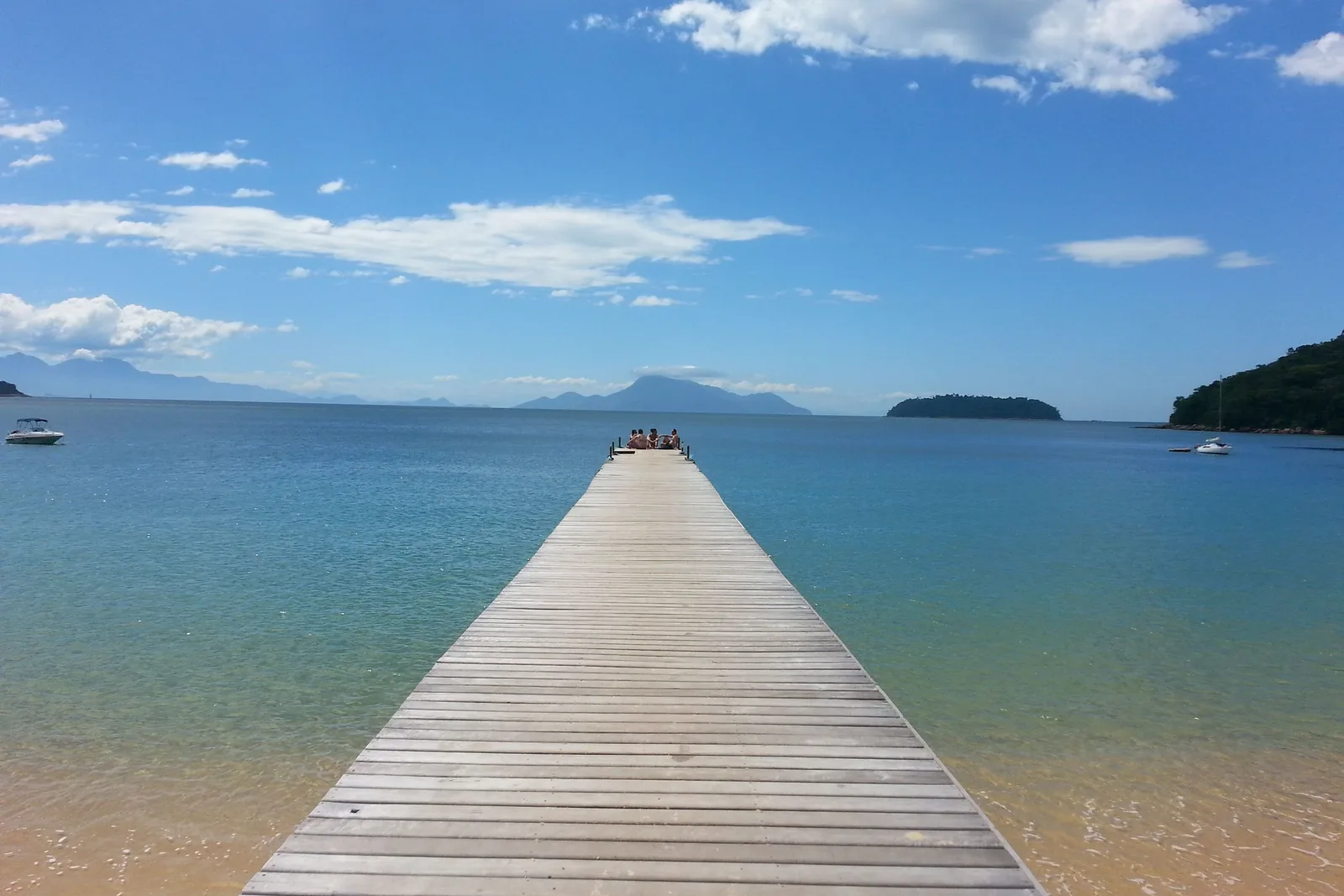 A long wooden pier running out over calm turquoise water at Praia de Palmas
