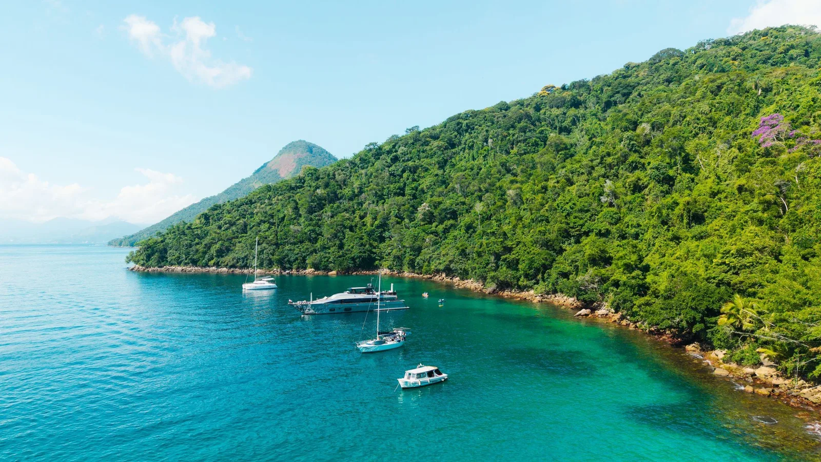 Ilha Grande from the air: boats at anchor on clear turquoise water below a steep forested shoreline