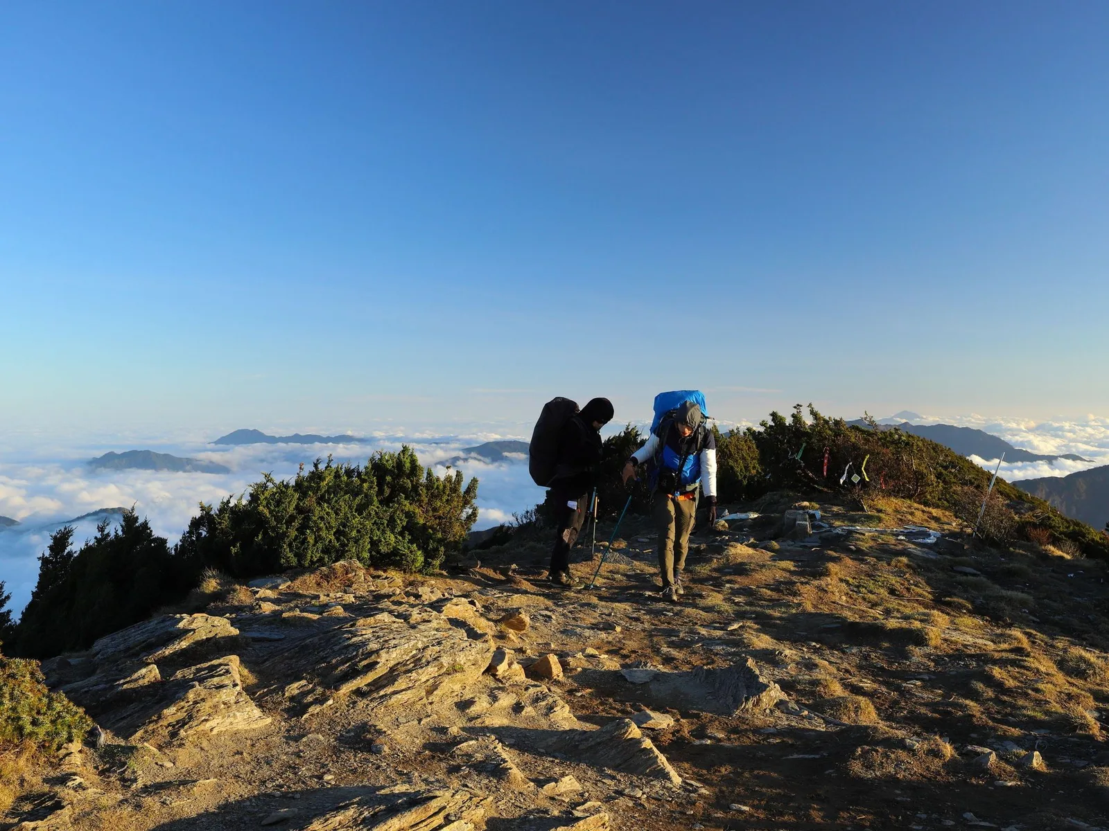 Two walkers on a ridge path in early morning light with cloud lying in the valley below