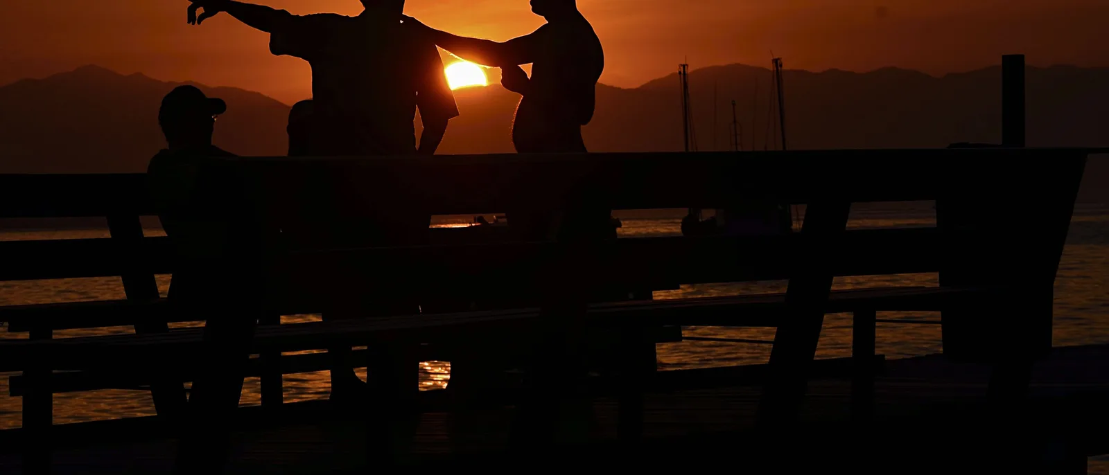 A wooden jetty running out from the beach at Araçatiba at sunset, people silhouetted along it