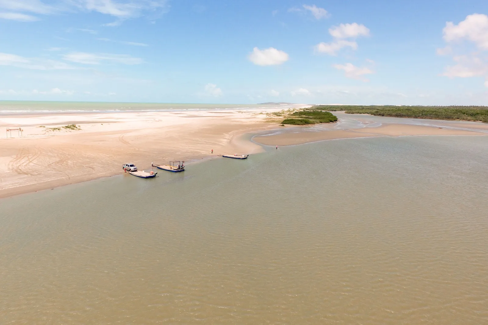 A wide shallow river mouth at Mangue Seco with small boats moored on the pale sand flats, low green scrub along the far bank and a big cloudy sky
