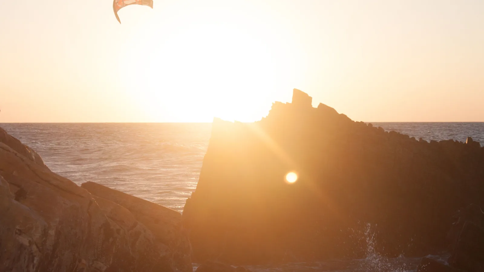 The sun blazing low beside the dark silhouette of Pedra Furada, the sea running gold in front of it and a single kite high in the sky above
