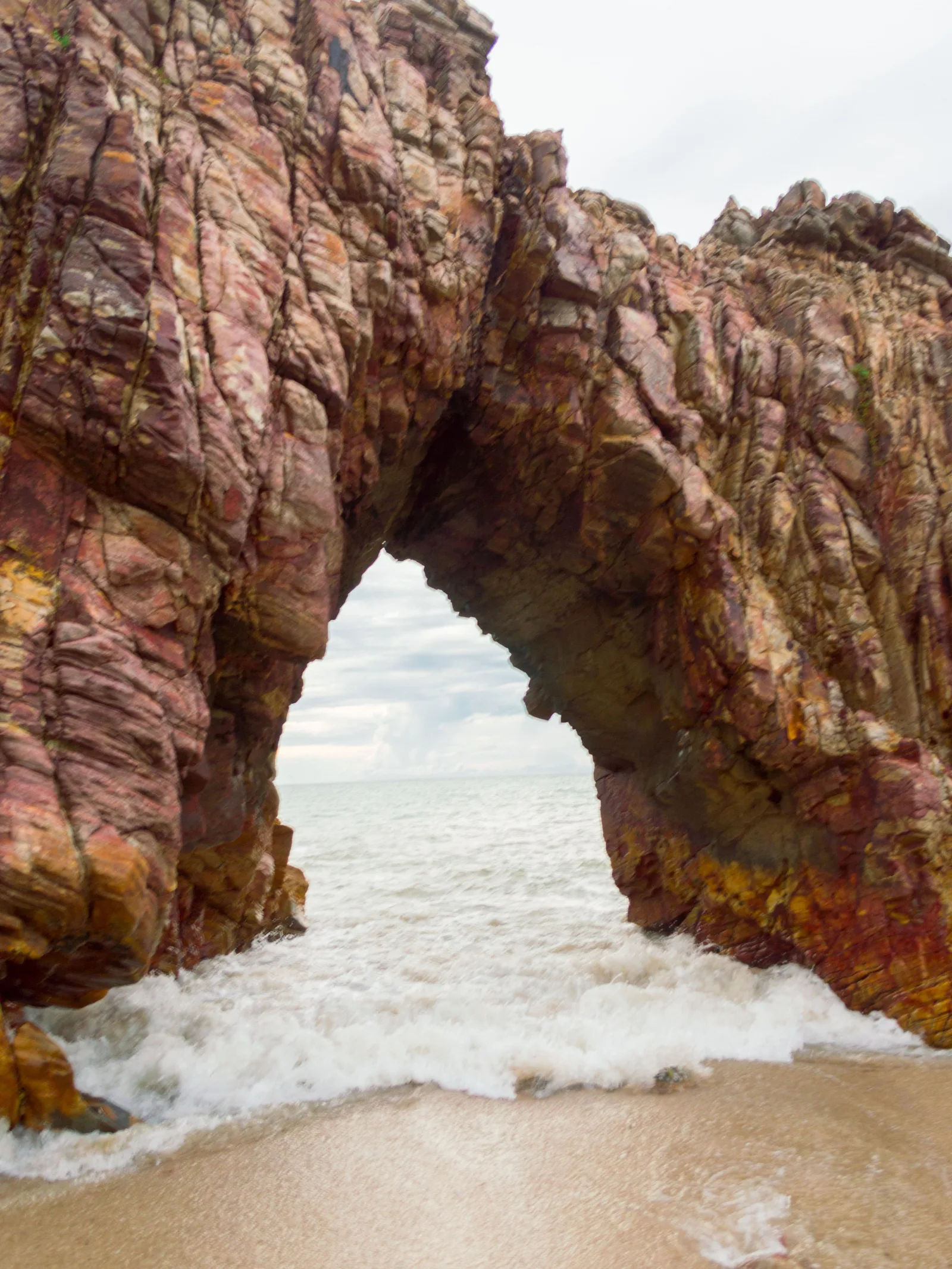 The Pedra Furada arch photographed from directly underneath: banded orange rock framing a bright rectangle of sea and sky