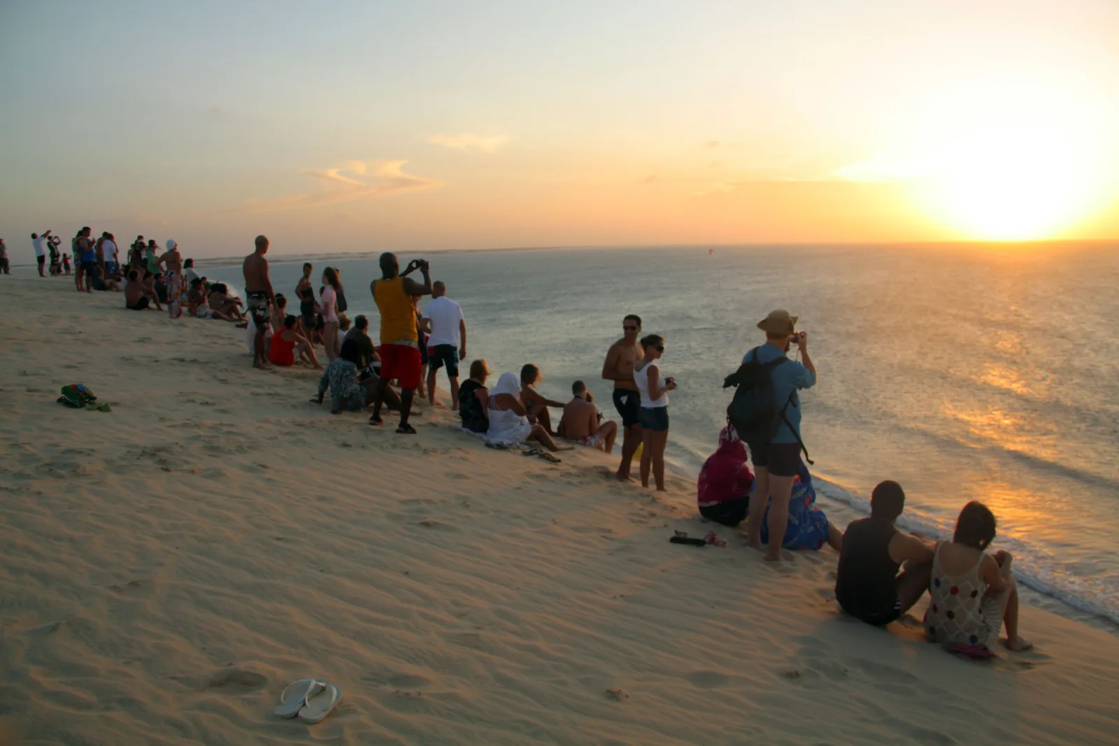 People sitting in rows on the sand of the sunset dune, looking out over the sea with the sun low on the horizon