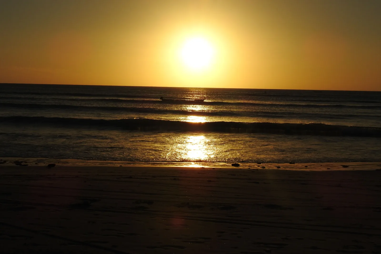 A gold path of low sunlight running across the sea toward the shore at Jericoacoara under a clear sky