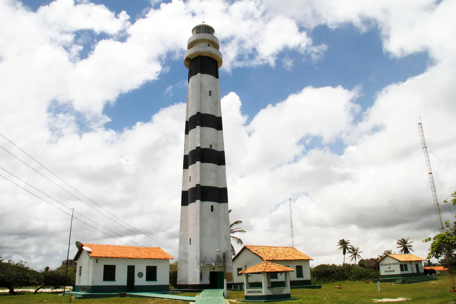 The Farol Preguiças seen from below against a sky of broken cloud, its black-and-white bands rising above the orange-roofed keepers’ cottages at its foot