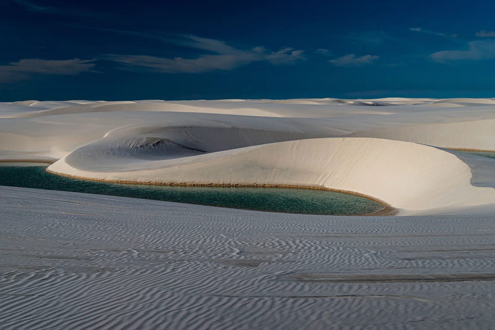 A steep white dune curving around a turquoise lagoon under a deep blue sky, the sand ridged by the wind