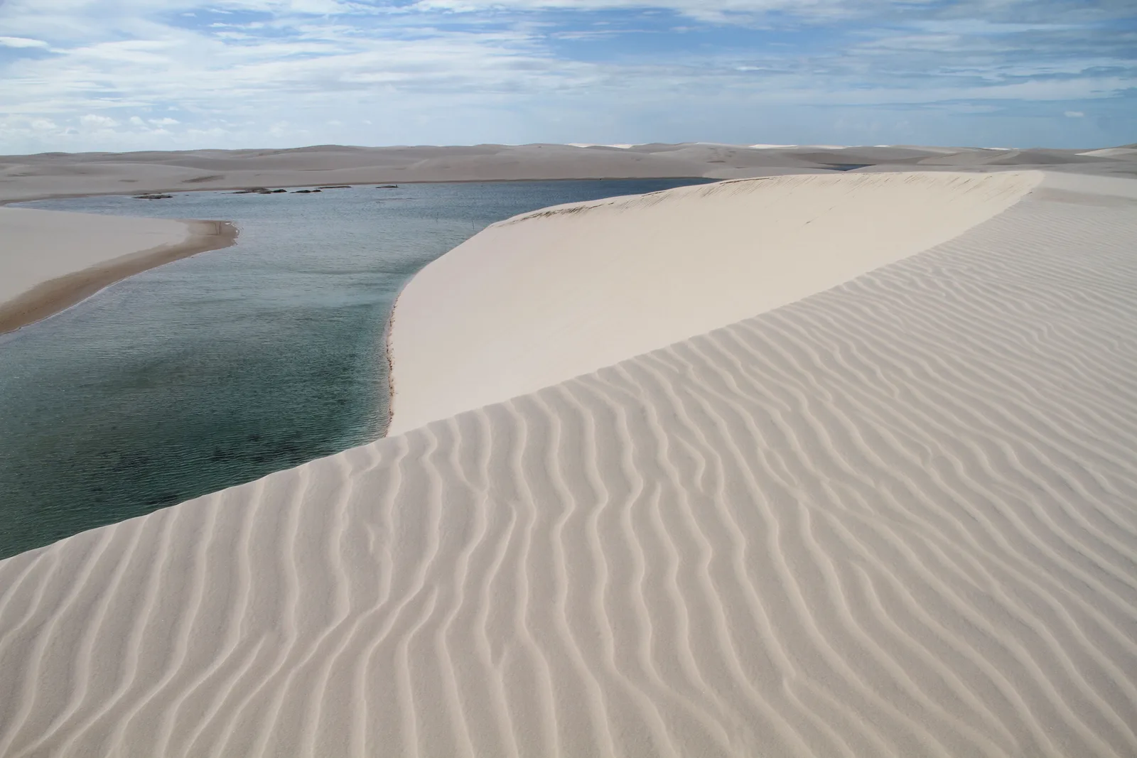 Wind ripples across the foreground sand and a lagoon curving around the foot of a white dune beyond it