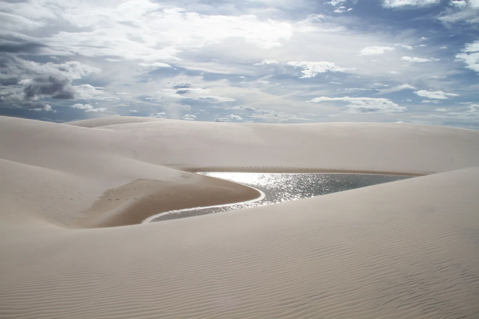 Late sun glinting off the surface of a lagoon set deep between two smooth white dunes