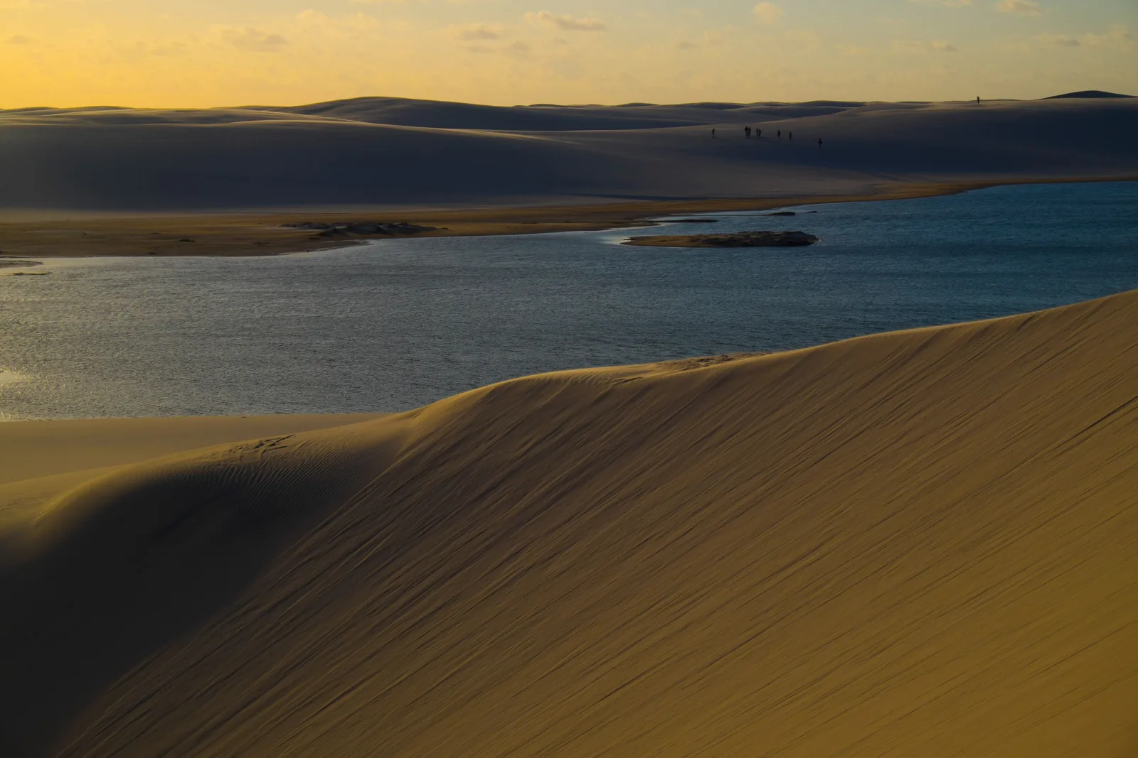A broad dark lagoon at the foot of a golden dune slope in late afternoon light at Lagoa Bonita