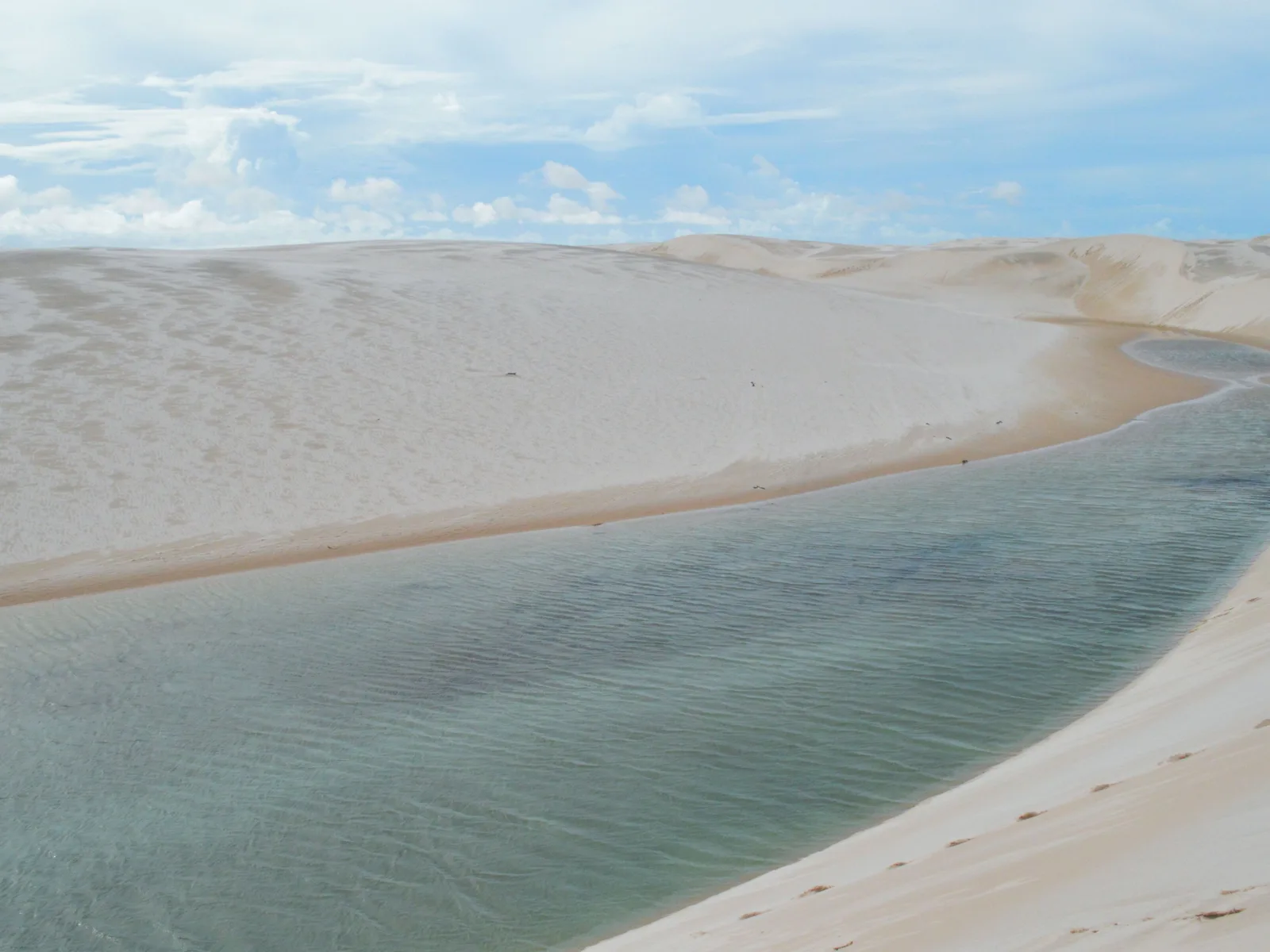 The pale turquoise edge of Lagoa Azul curving along the foot of a smooth white dune under a bright hazy sky