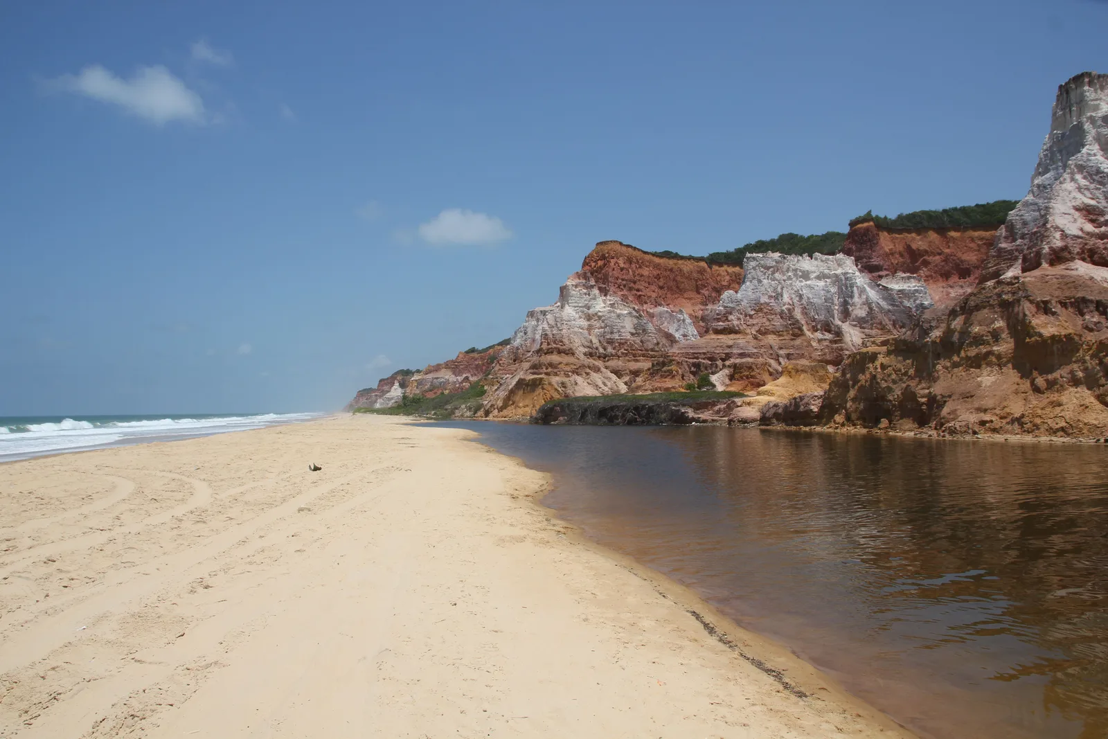 The colored cliffs at Gunga rising directly behind the beach, with the dark lagoon channel running along the sand in front of them