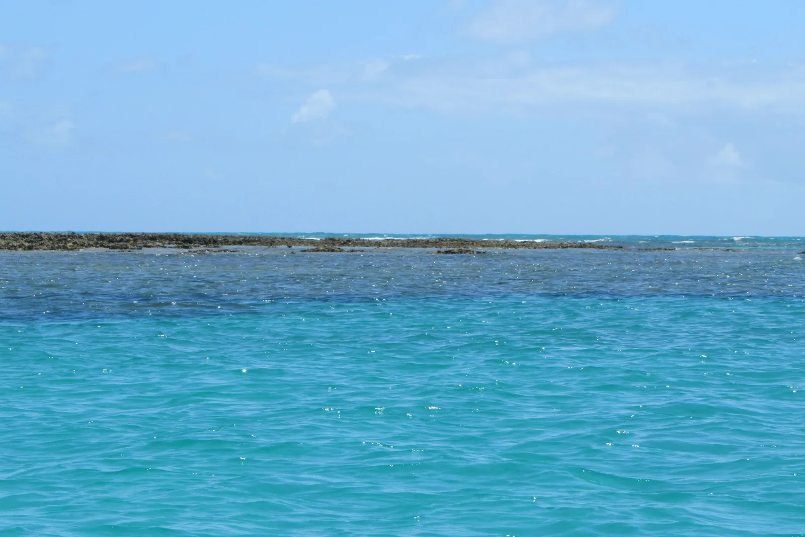 The reef off Maragogi breaking the surface of flat turquoise water in a long dark line, with open sea and a band of white surf beyond it and no land in sight