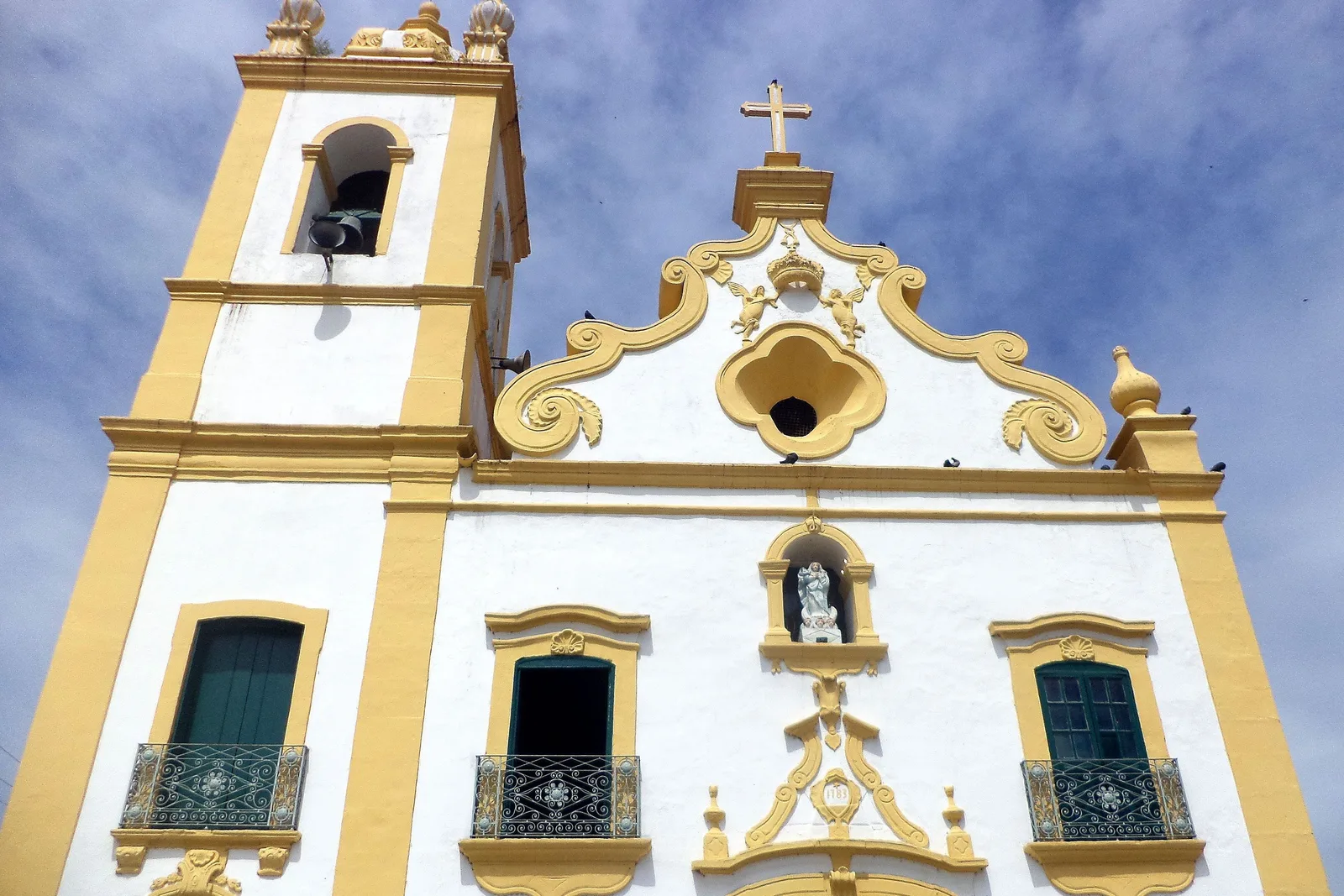 The baroque front of the parish church at Marechal Deodoro in white and gold, its curved gable and bell tower against a blue sky