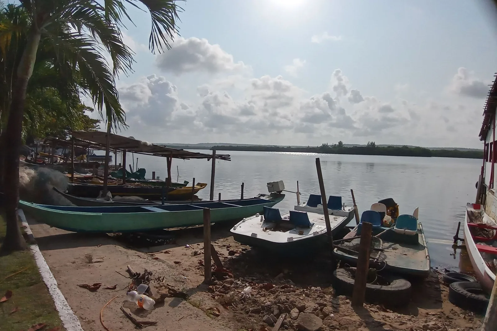 Wooden fishing boats pulled up on the muddy lagoon shore at Pontal da Barra, nets and gear in them, palms and low houses along the far bank