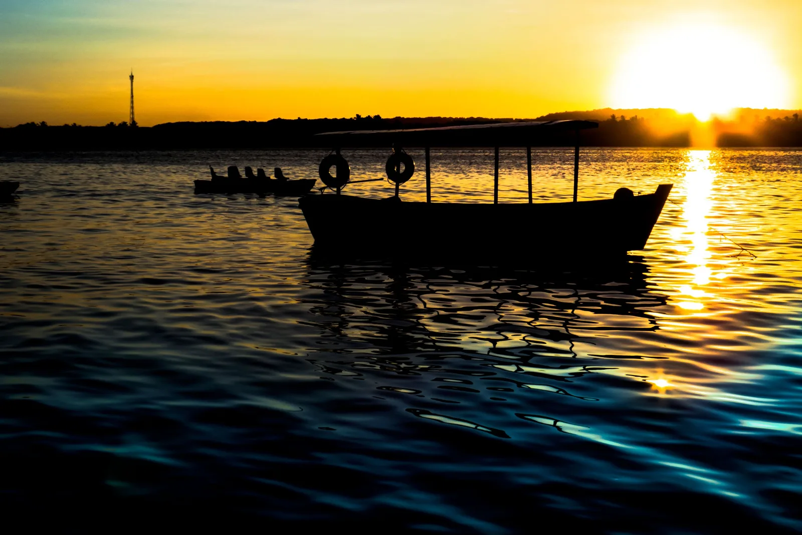 Sunset over the lagoon at Pontal da Barra, a moored boat in silhouette on gold water