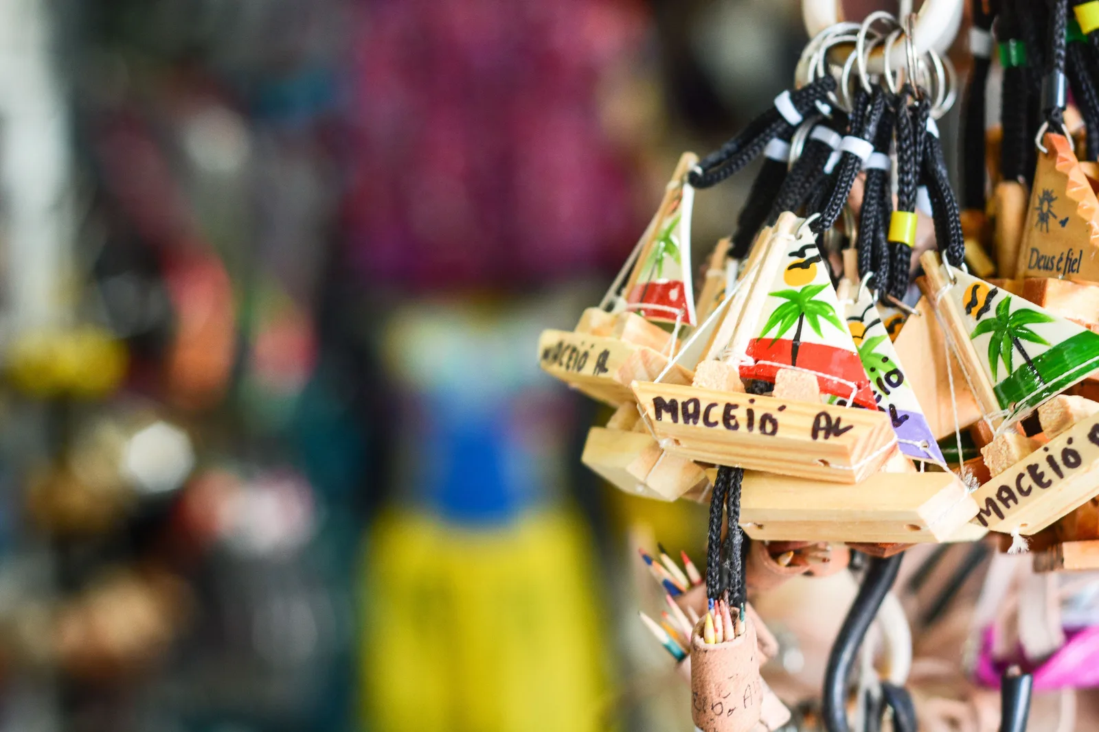 Wooden keyrings painted with beach scenes and the word Maceió, hung in rows on a market stall