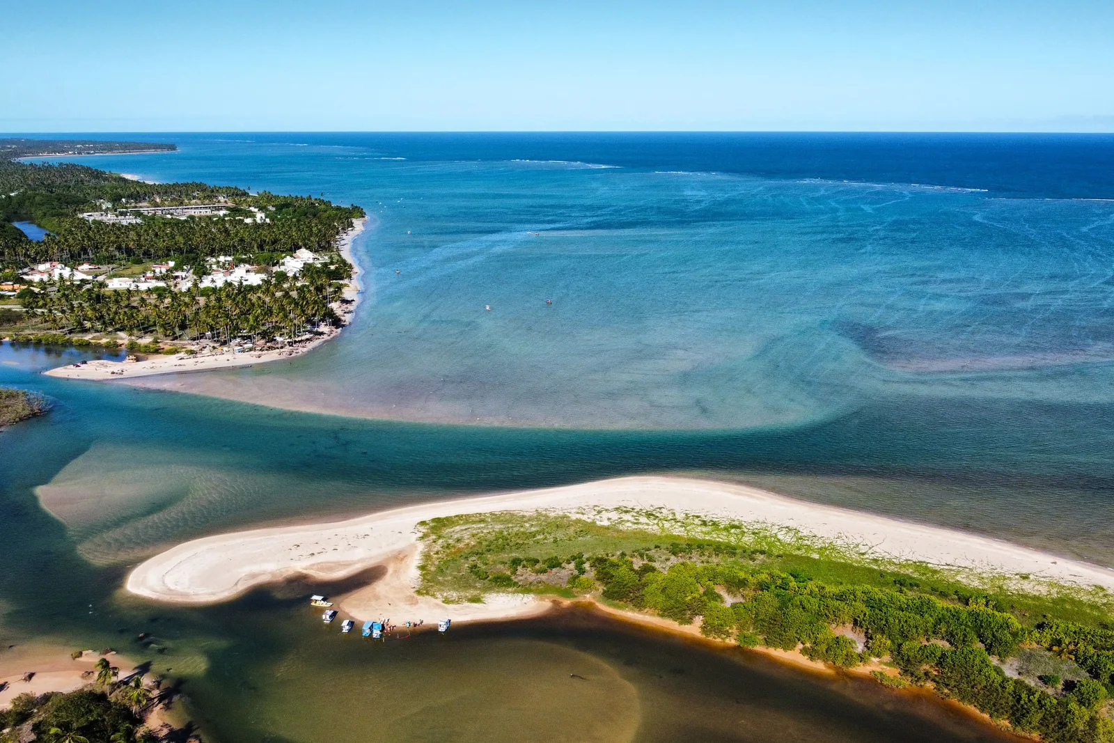 The mouth of the Riacho Tabatinga from the air: a river running out through a pale sandbar into a turquoise reef lagoon