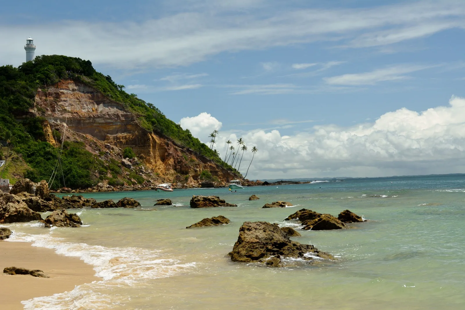 The eroded headland at Morro de São Paulo seen from the sand of Primeira Praia, the small white lighthouse standing on the ridge at the top and the zipline cables running down the cliff face to the water