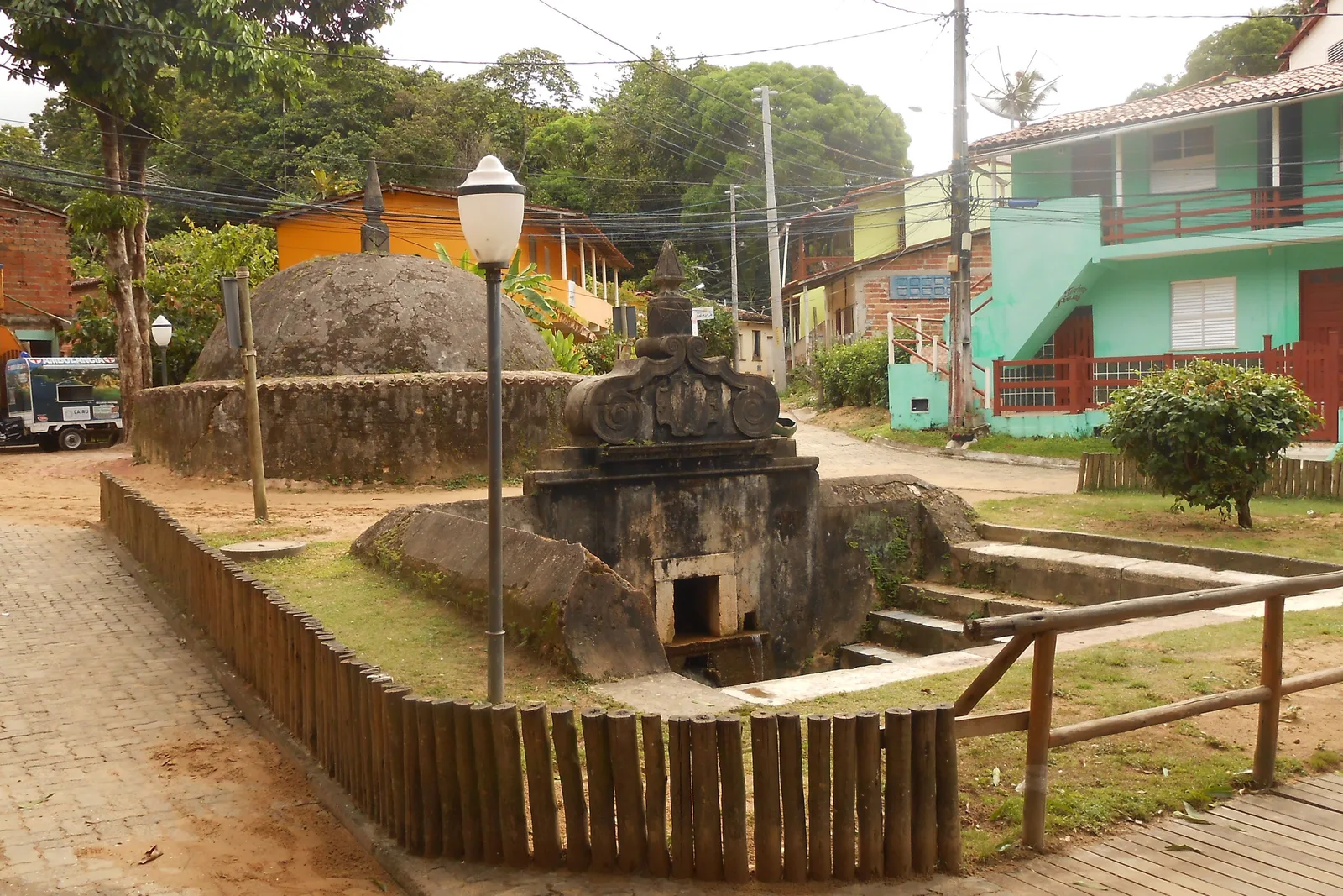 The Fonte Grande in Morro de São Paulo, a low stone fountain building with a carved pediment set in a paved sunken square, houses and a lamp post behind it