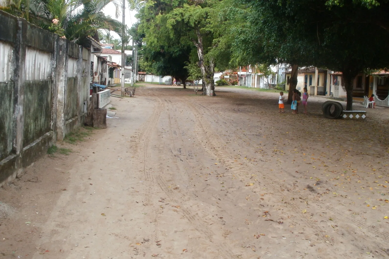 A wide sand street in the village of Gamboa, low houses and a wall along one side, trees down the middle of it and a handcart standing in the road