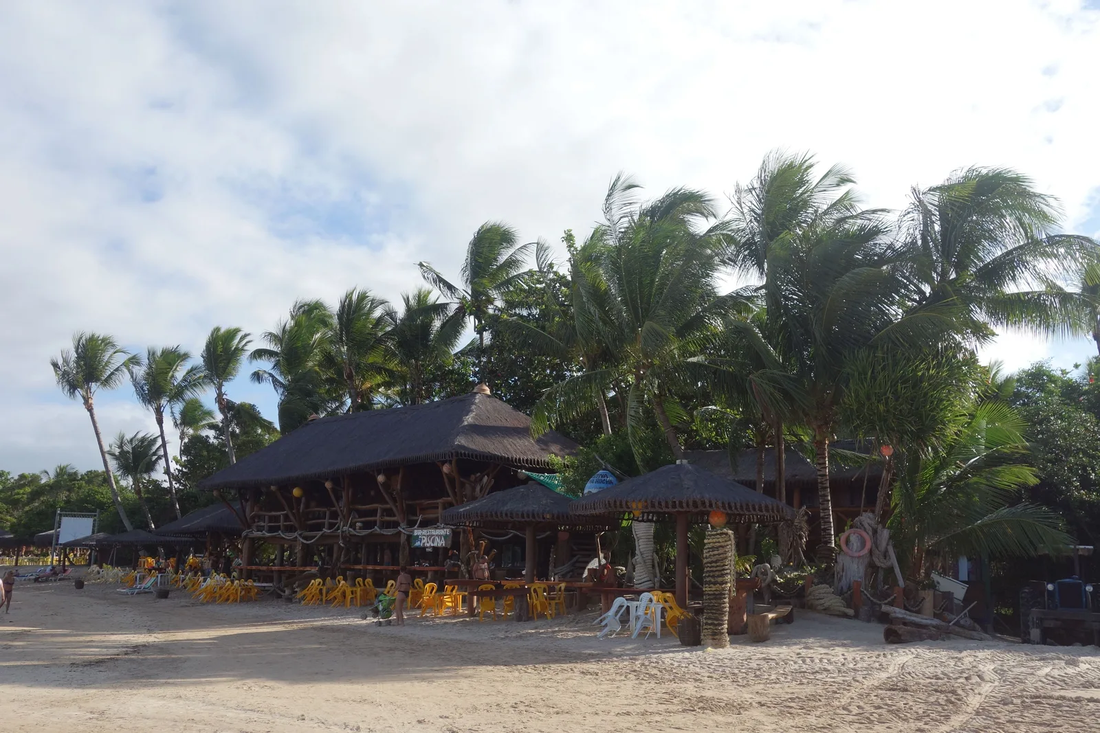 A thatched beach bar set back under coconut palms on the sand at Morro de São Paulo, tables and kayaks out in front of it