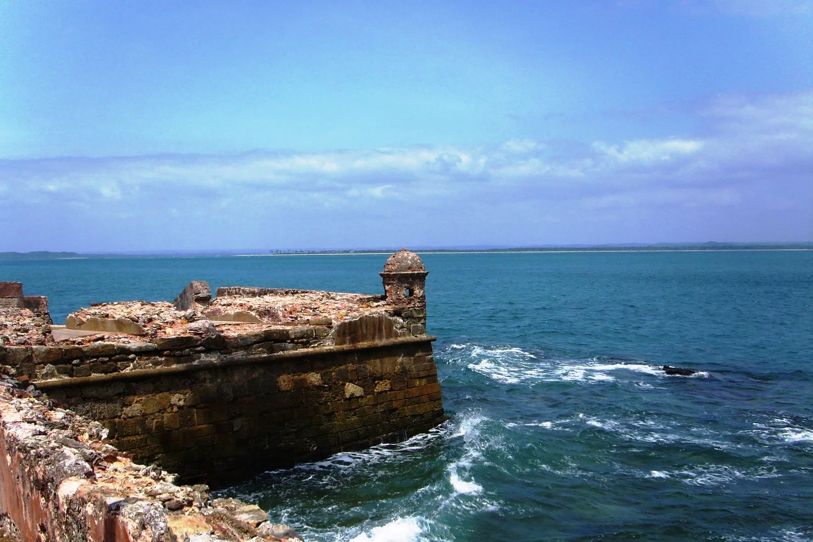 A stone sentry box on the sea wall of the Fortaleza de Tapirandu, standing over surf breaking on the rocks below