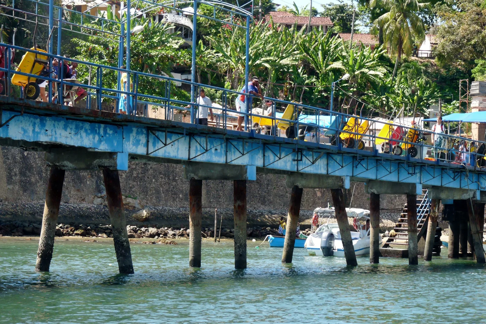 The landing pier at Morro de São Paulo busy with arriving passengers, stalls and awnings along its length and boats tied up either side