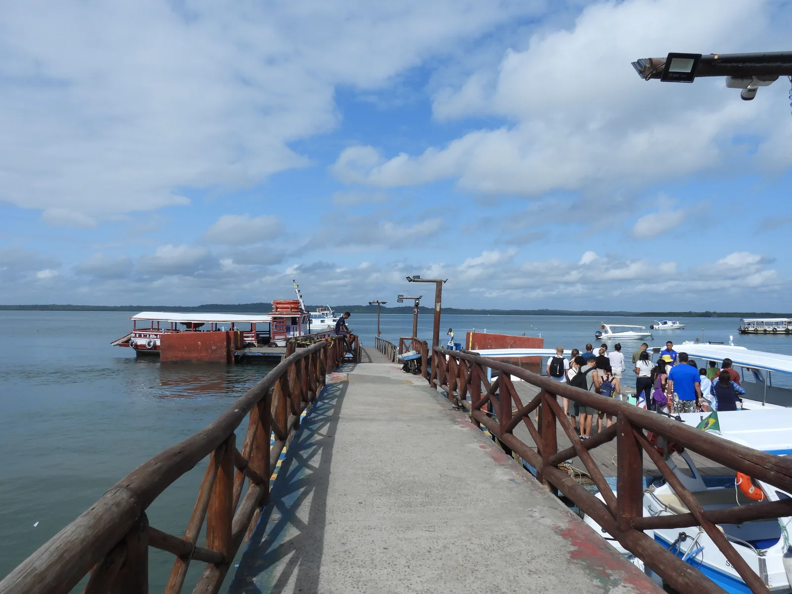 The pier at Morro de São Paulo from the causeway, passengers walking in from the boats with the low green shoreline of the village beyond