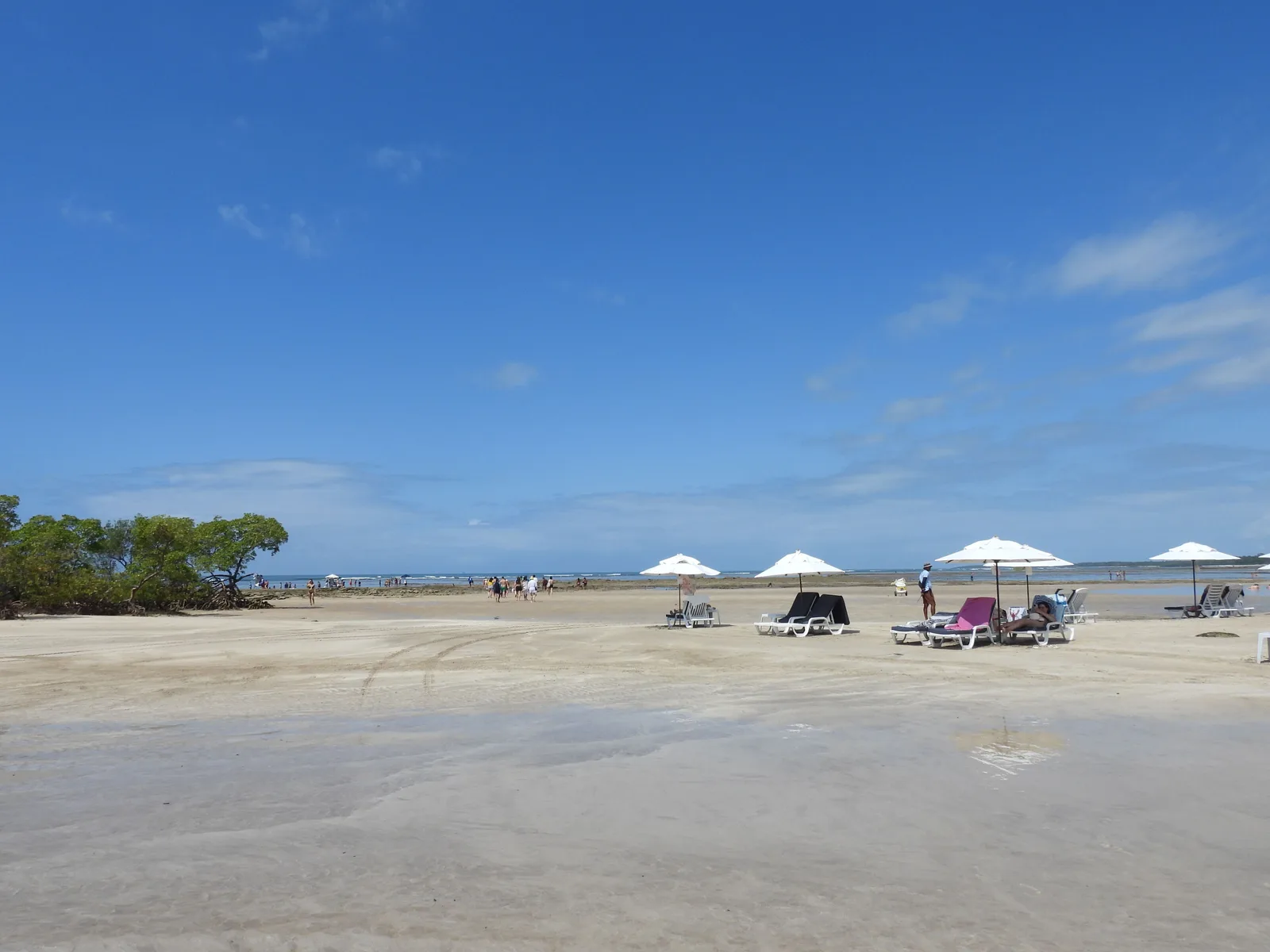 A broad empty beach at Morro de São Paulo at low tide, loungers and white umbrellas folded along the back of the sand and the sea a long way out