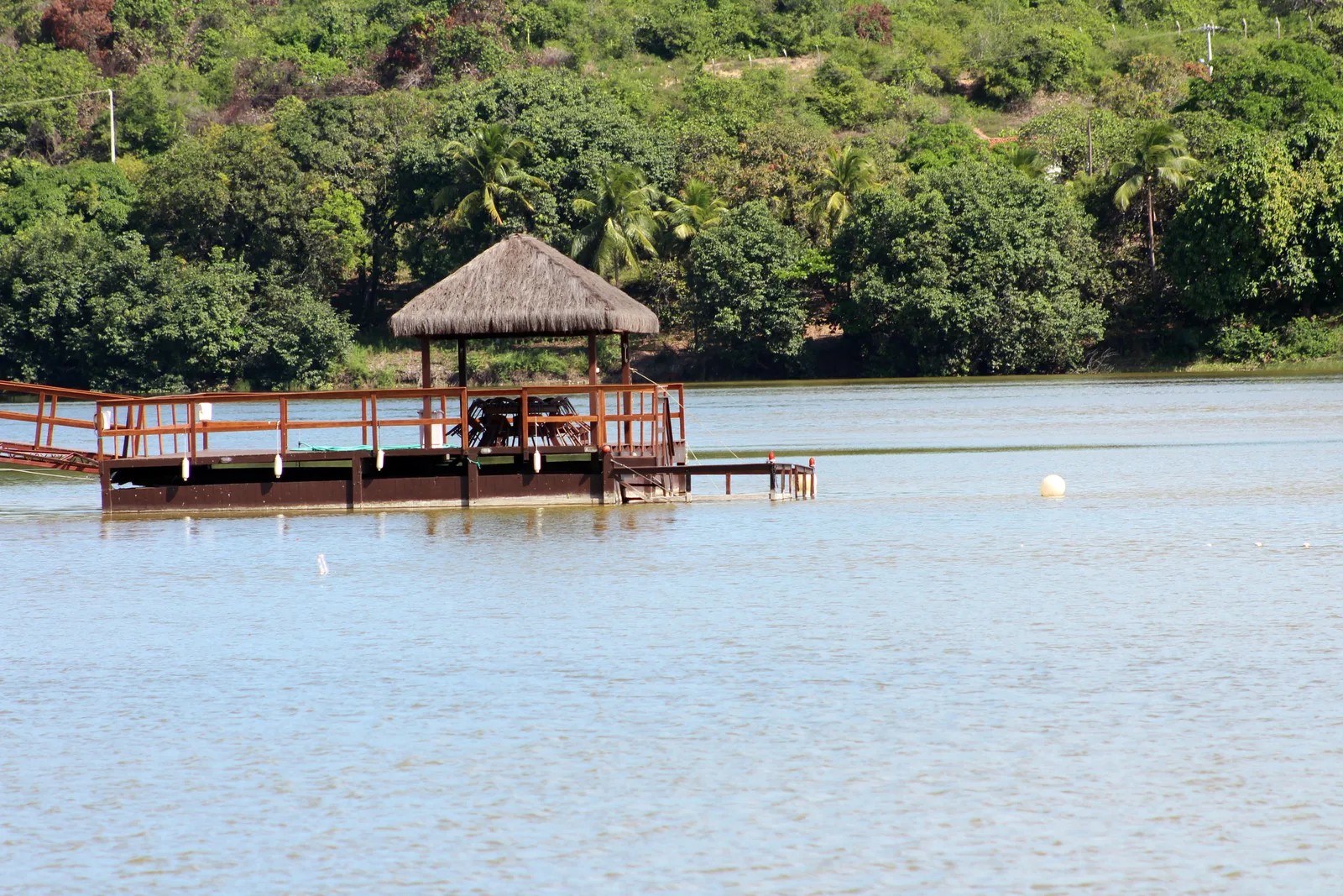A thatched wooden deck built out over the still water of the Lagoa de Extremoz, with dense green forest along the far shore