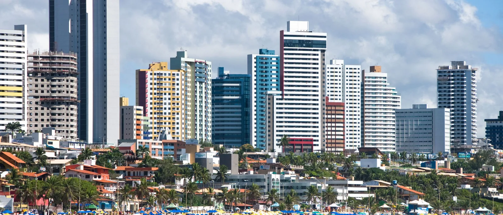 A wall of apartment and hotel towers at Ponta Negra rising above the low red-tiled roofs and trees at their feet