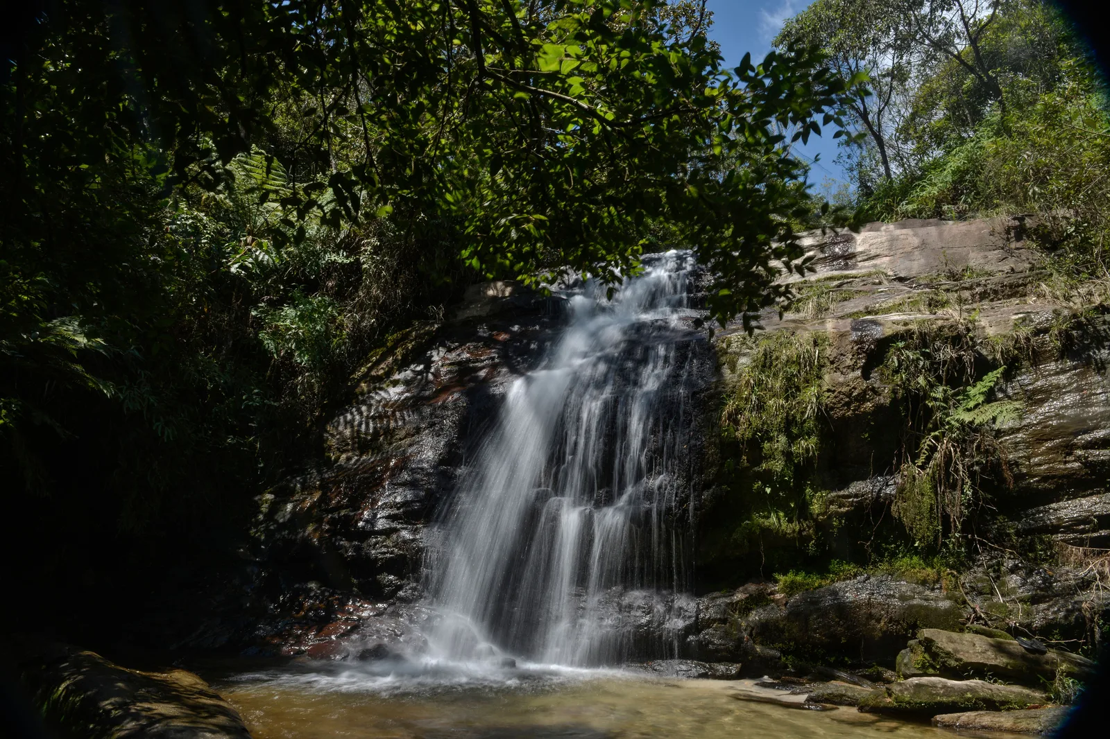 A waterfall dropping in several steps down a dark rock face into a shallow pool at Lavras Novas, dense green forest closing in on both sides