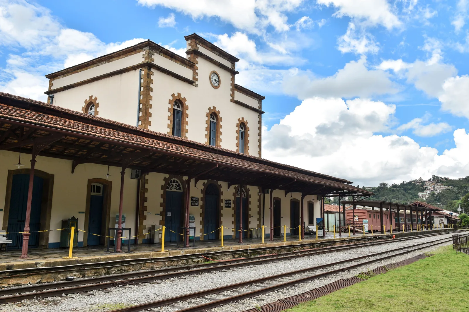 The empty platform of Ouro Preto’s train station under a bright sky, a long white station building with arched windows and a canopy along one side and the rails running away into the distance