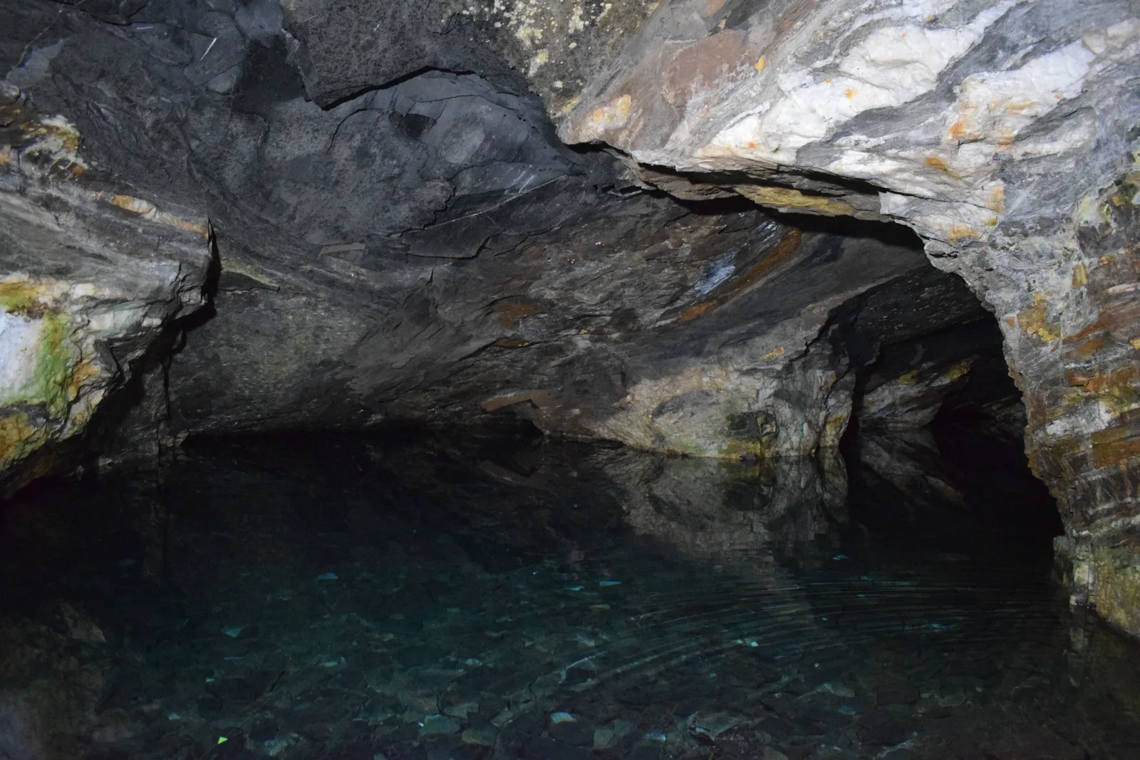 The underground lake inside Minas da Passagem near Mariana, clear blue-green water filling the floor of a dark rock cavern lit from one side, the mine roof arching low over it