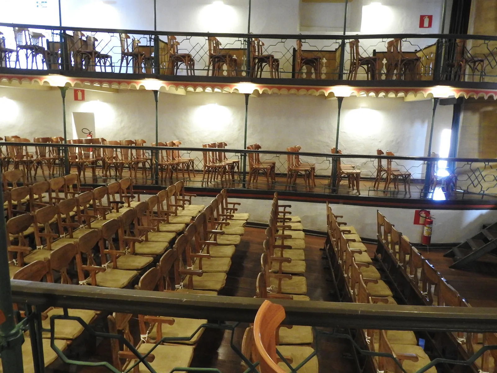The wooden auditorium of the Casa da Ópera in Ouro Preto seen from an upper box, rows of chairs on the raked floor below and curved balconies with iron railings running around three sides
