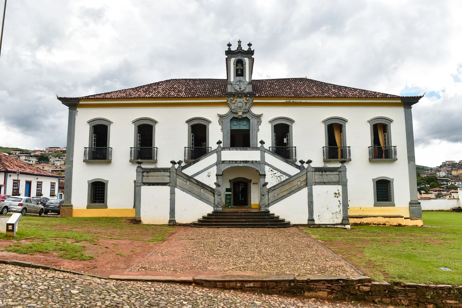 The Casa de Câmara e Cadeia in Mariana: a long white colonial building with a yellow base, a small belfry on the roof and a symmetrical double stone stairway climbing to the front door
