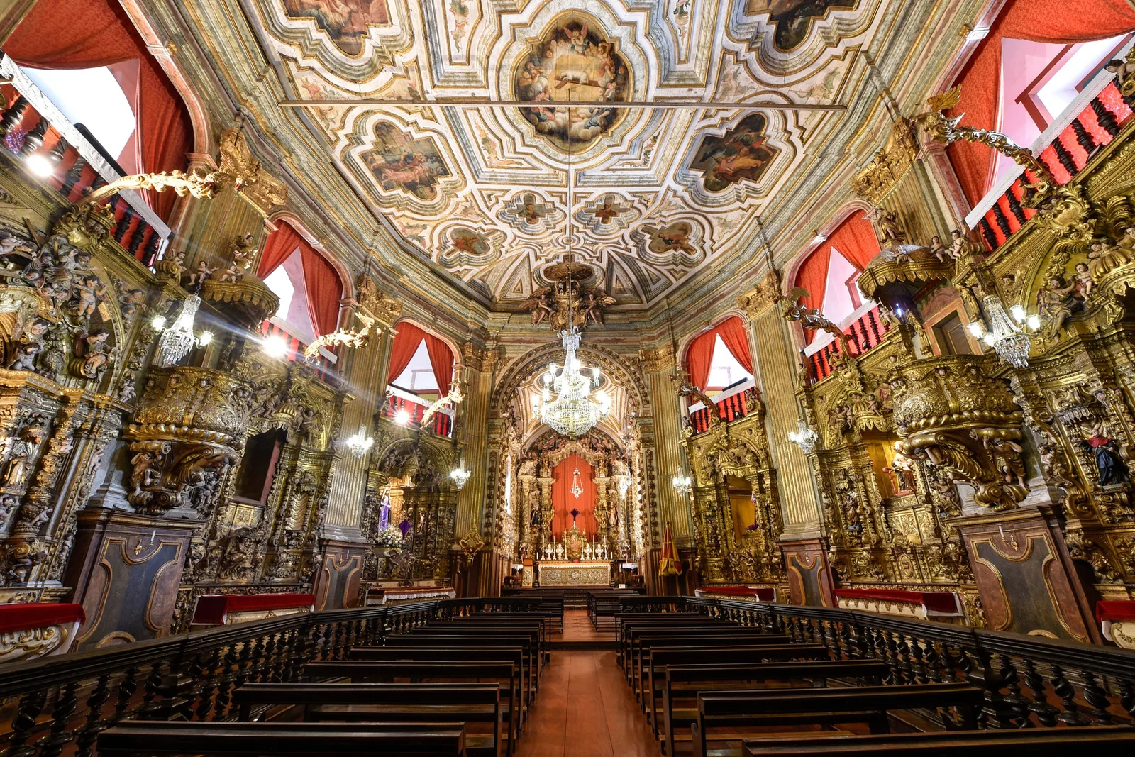 Inside the Matriz de Nossa Senhora do Pilar: a polygonal nave lined floor to ceiling with gilded carving, red and white drapery hung between the arches, and a painted ceiling above the pews