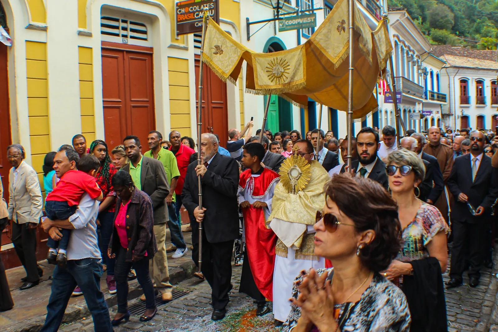 The Resurrection procession at Easter in Ouro Preto: a gold canopy carried over the clergy down a cobbled street between yellow and white colonial houses, with a crowd walking behind