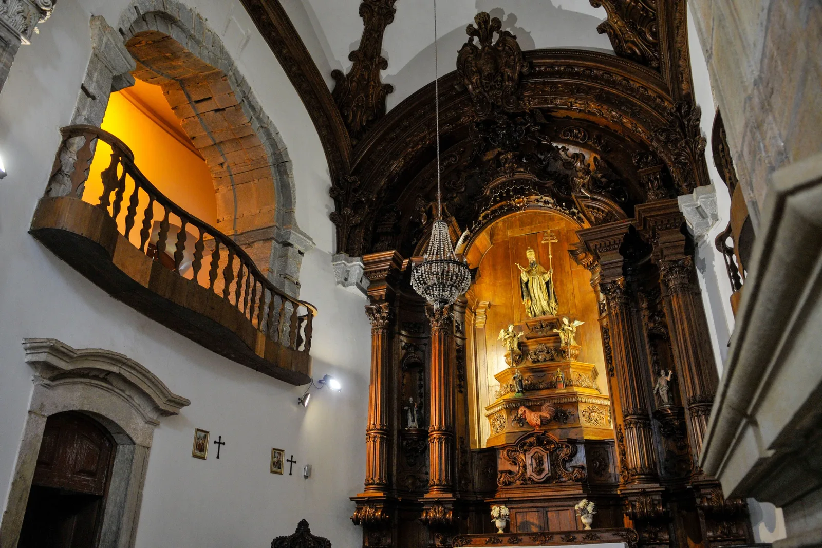 The gilded interior of the Igreja de São Pedro dos Clérigos in Mariana, a lit altar under a carved arch and a wooden tribune balcony running above the nave