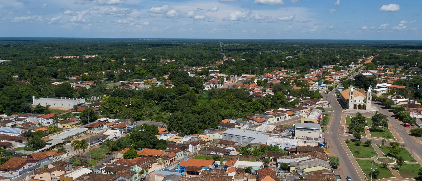 Aerial view of a small town of red-tiled roofs and low buildings around a church, with green countryside running to the horizon