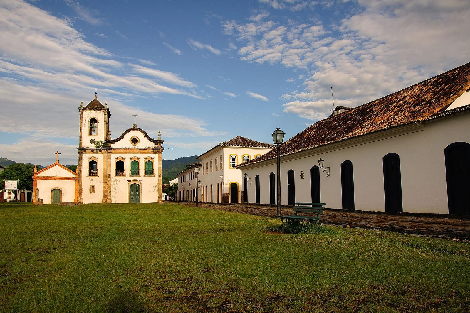 The whitewashed Igreja de Santa Rita seen across the grass at the edge of the waterfront, its single bell tower and dark wooden doors against a bright sky, forested mountains behind
