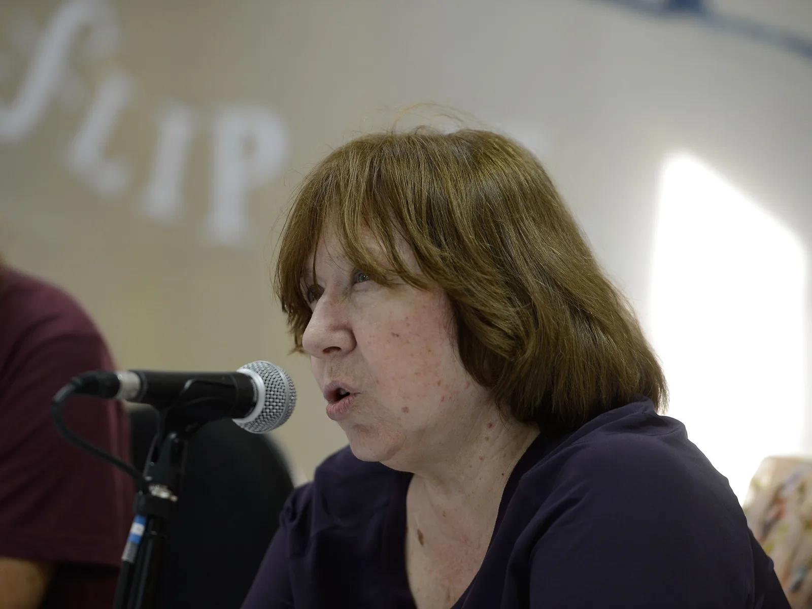 An author speaking at FLIP, Paraty’s international literary festival, a microphone in front of her and the festival lettering on the wall behind