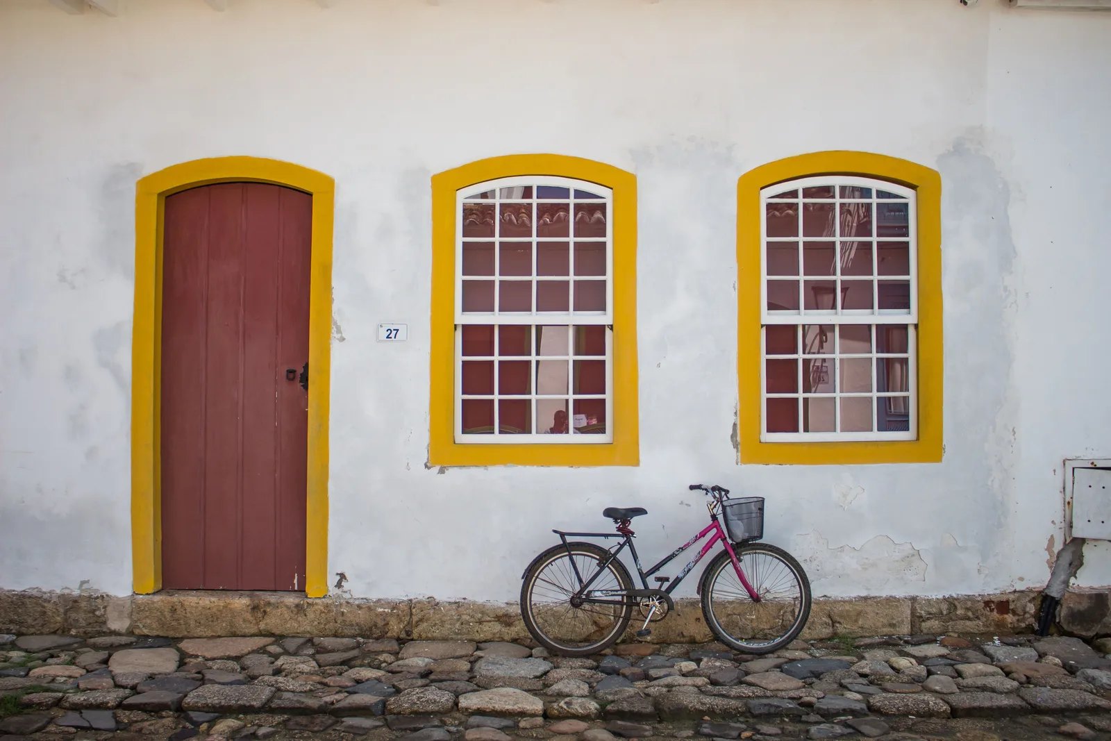 A bicycle leaning on a white wall under yellow-framed windows and a red door in the historic center