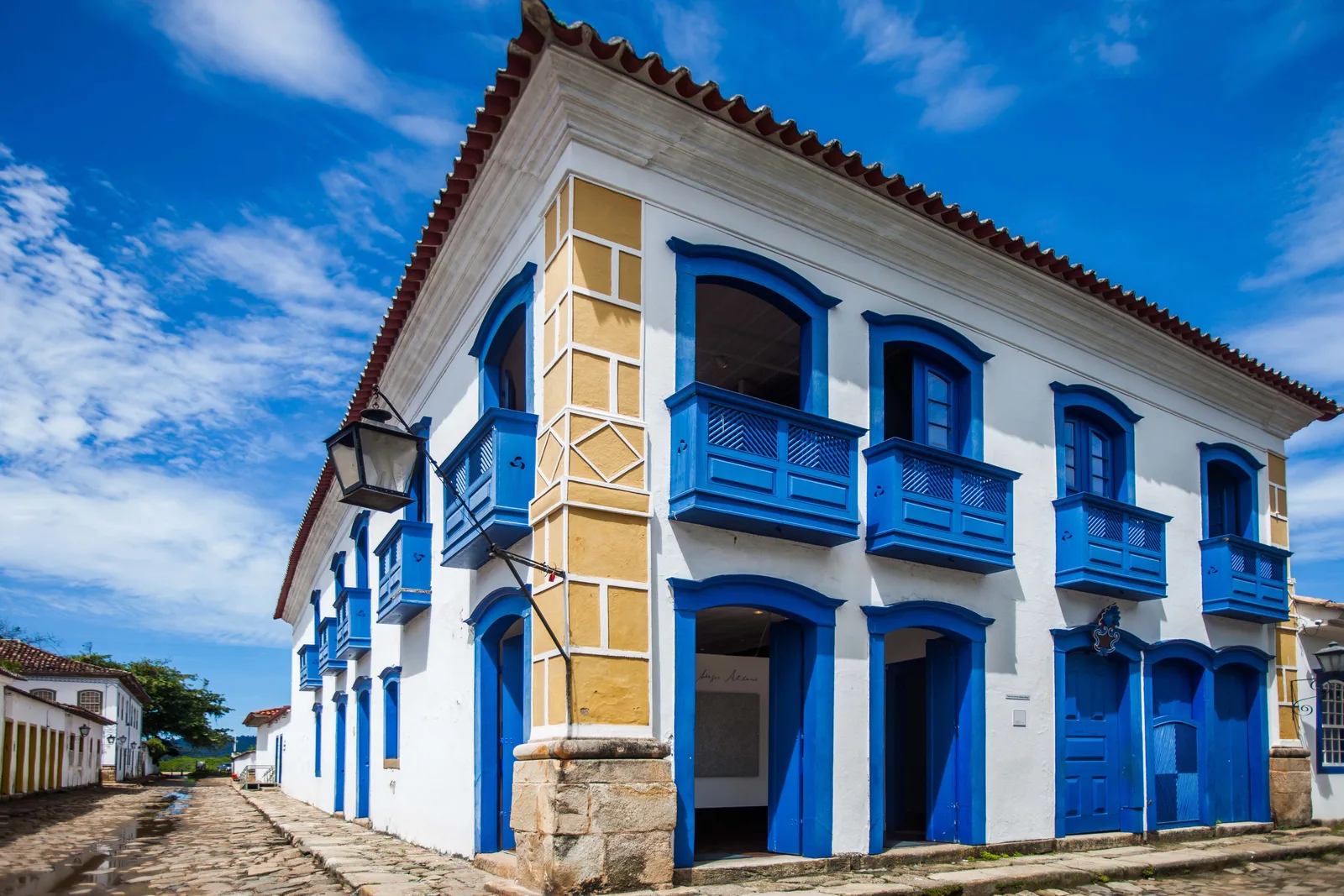 A two-story colonial corner house with bright blue balconies, doors and shutters, on a cobbled street