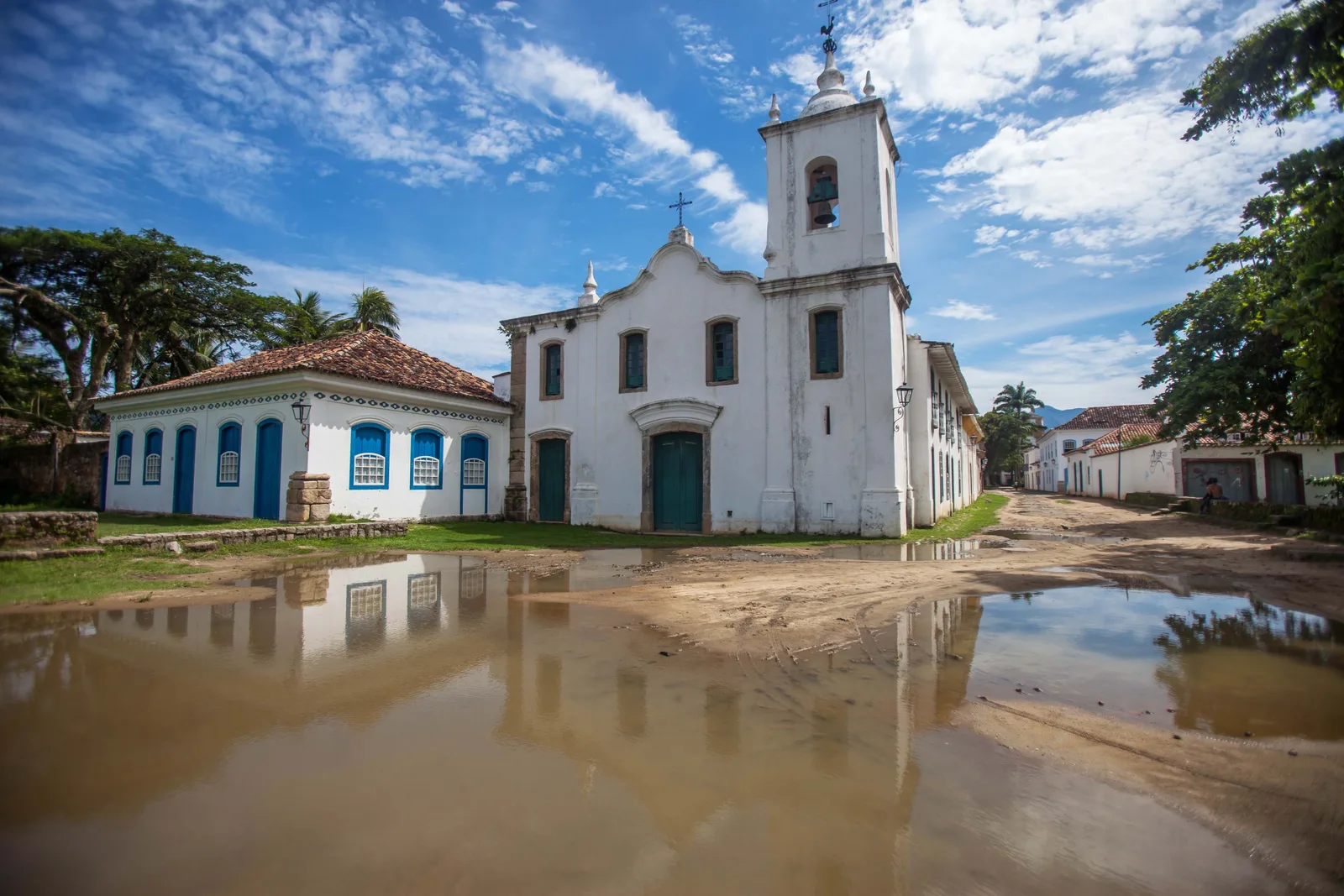 A white colonial church and its bell tower reflected in a rain puddle on a quiet street