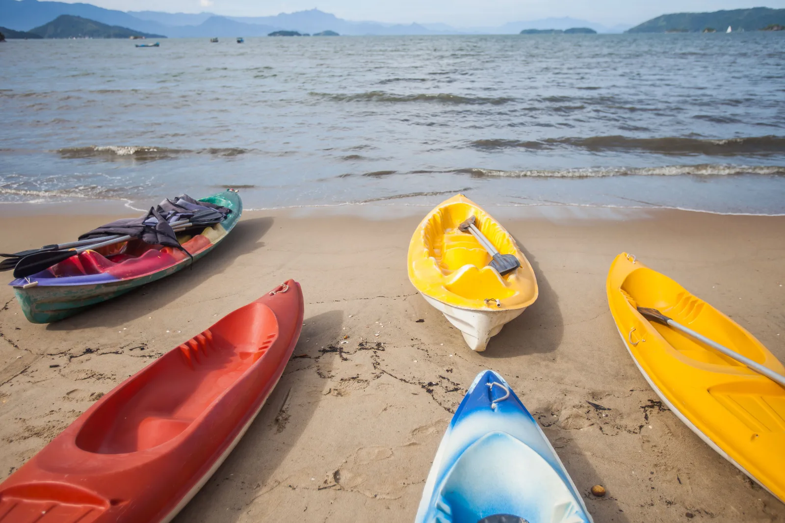 Bright red, yellow and blue sea kayaks pulled up on the sand at Praia do Pontal, islands on the bay behind