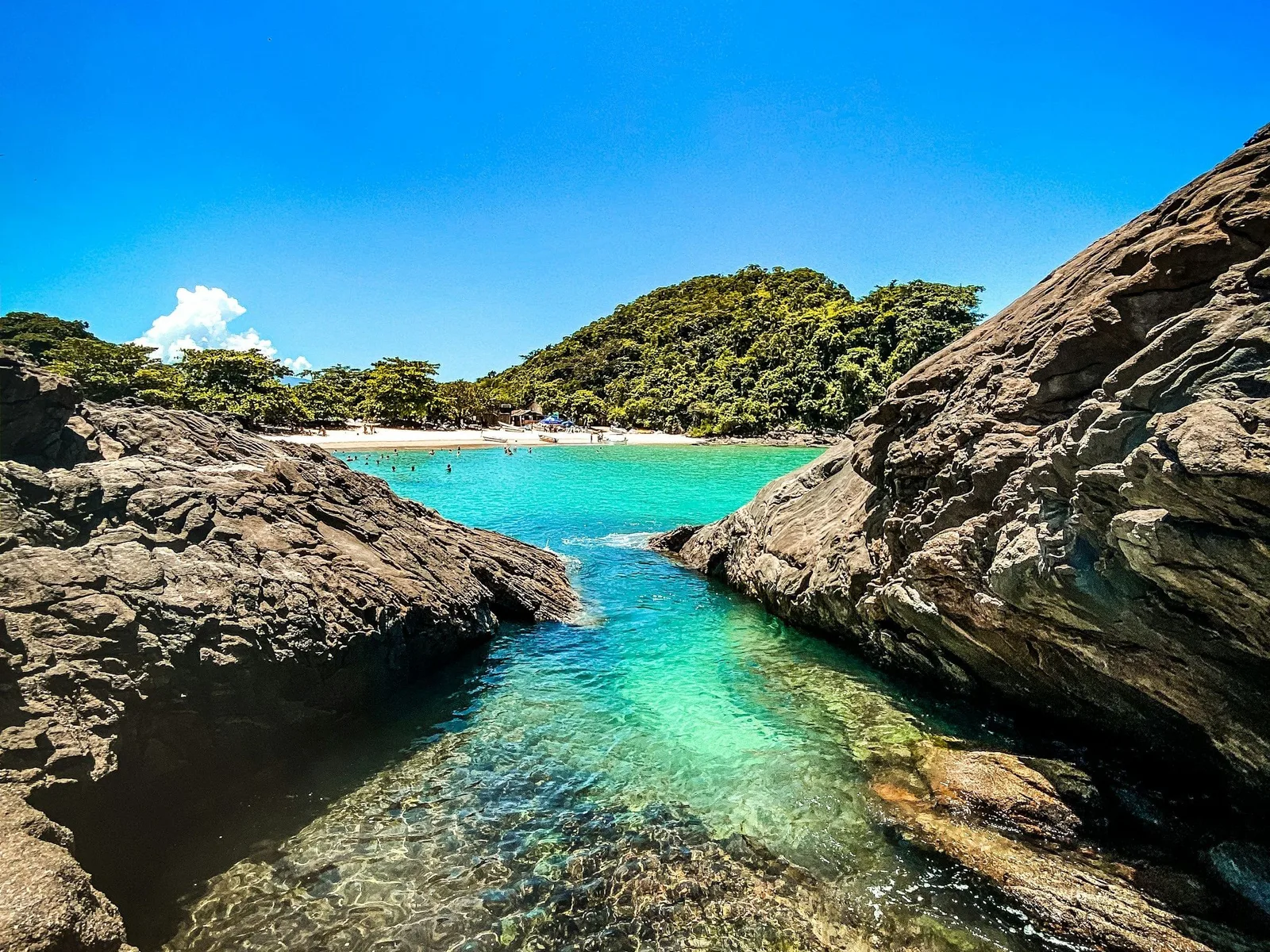 A narrow channel of clear turquoise water between granite outcrops in Paraty bay, forest coming down to the rock on both sides
